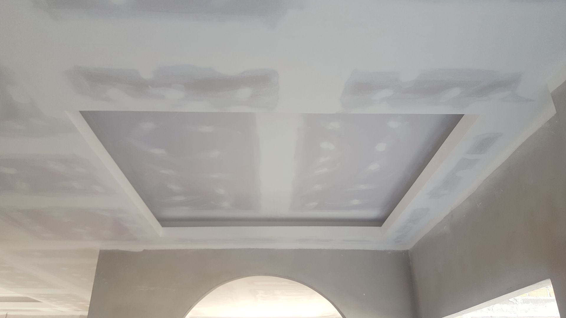 Tray ceiling with recessed rectangular panels and an arched opening below in a light gray room