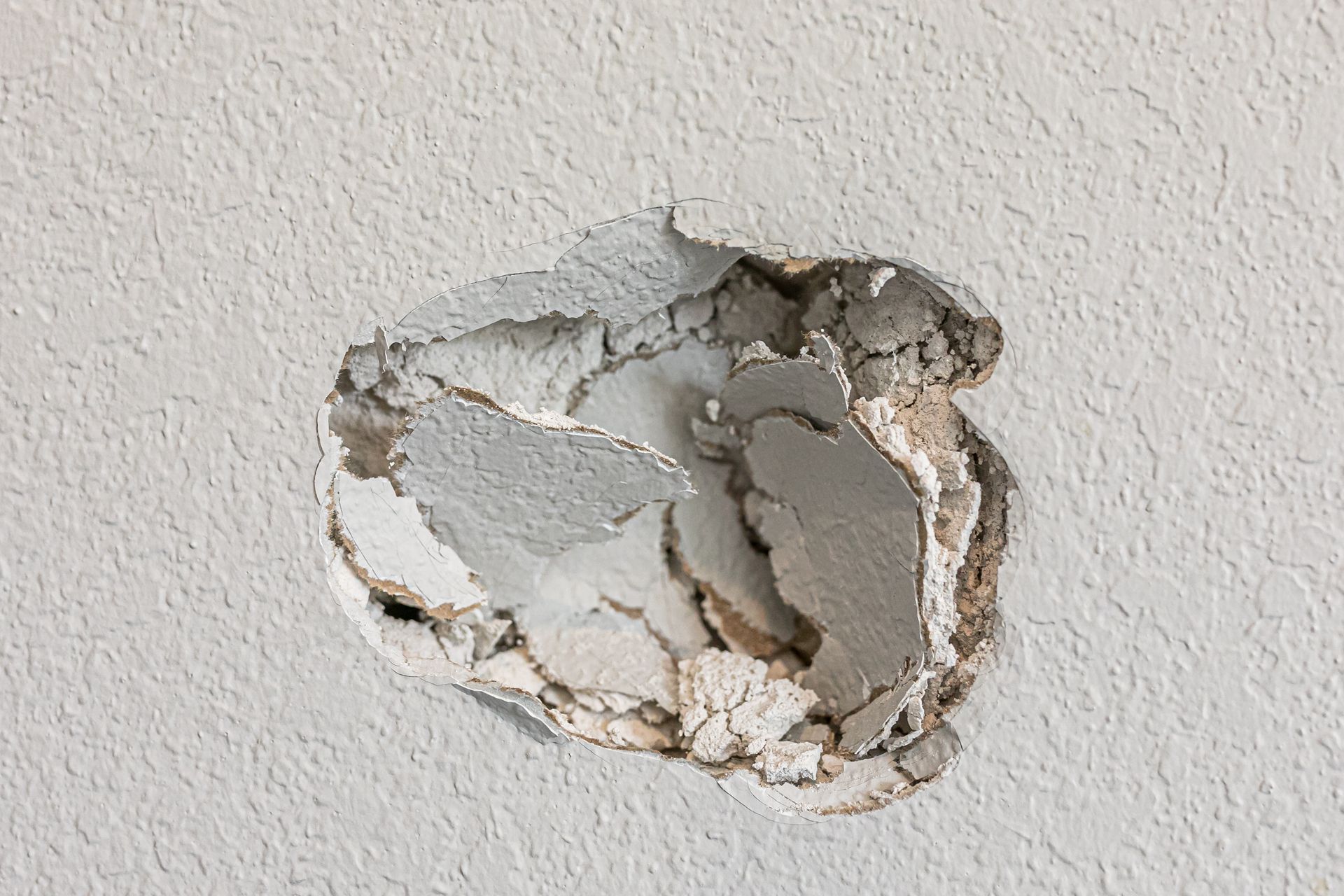 Peeling white wall paint revealing damaged plaster underneath