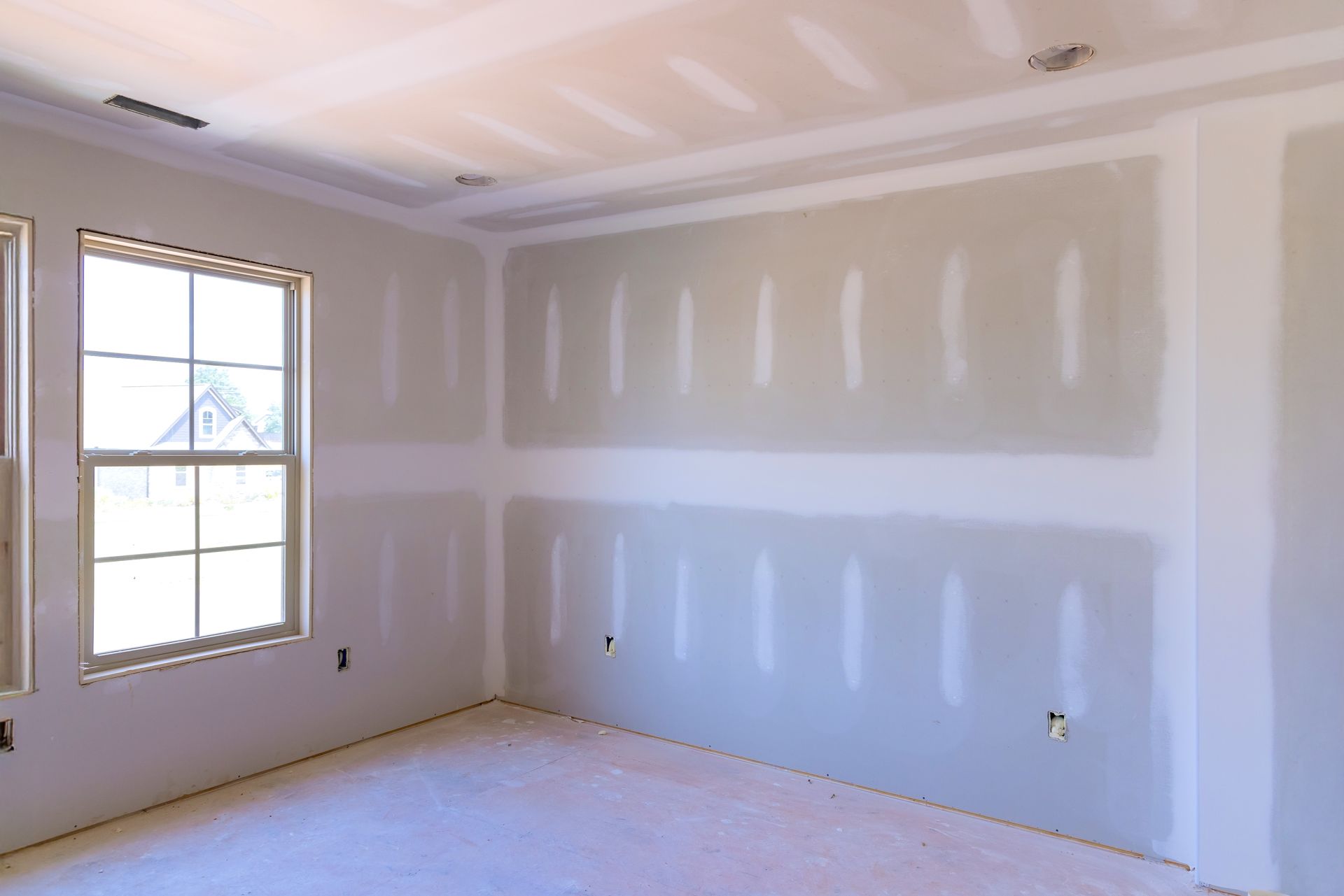 Empty drywall room with white walls, unfinished ceiling, and a window letting in daylight