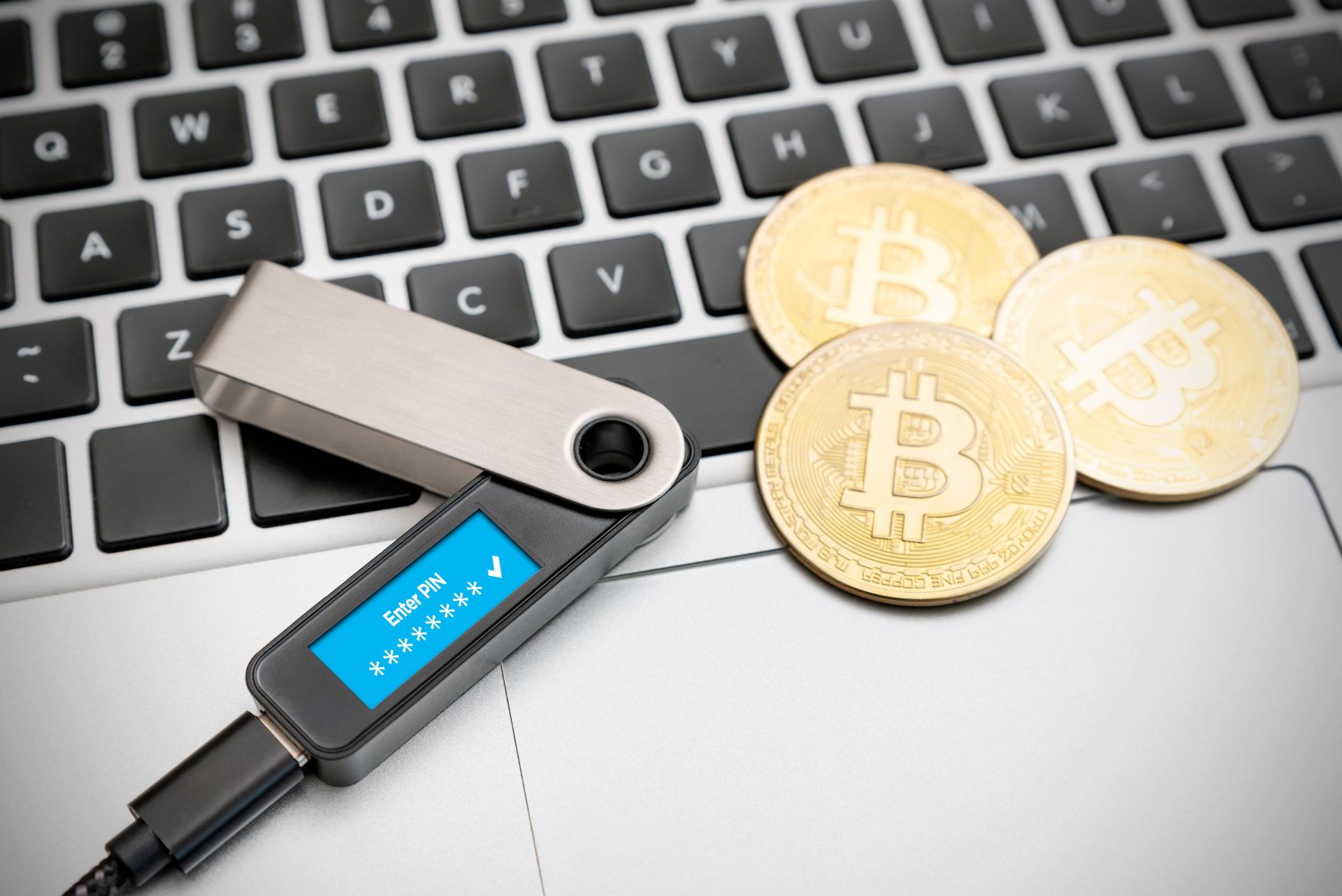 Bitcoin hardware wallet connected to laptop beside gold Bitcoin coins