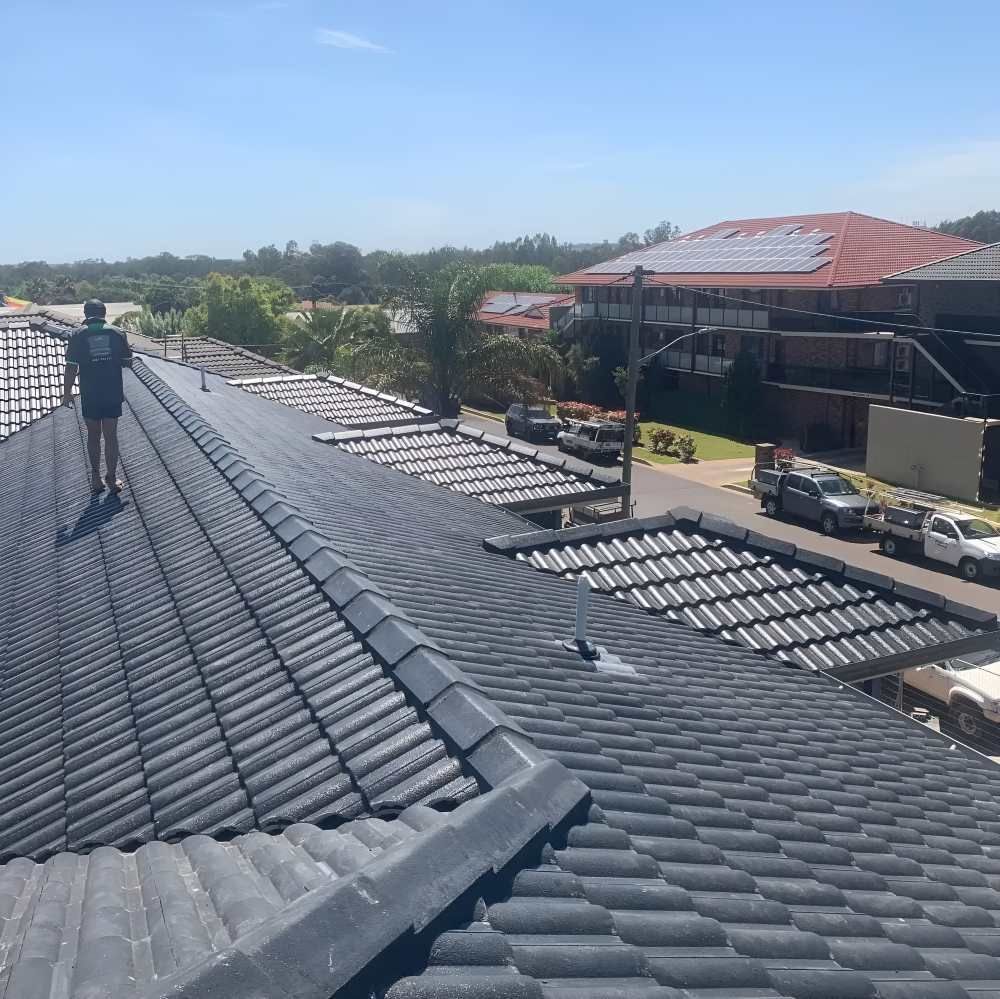 A Man Is Standing On Top Of A Tiled Roof — Lance Ward Roof Tiling in Forbes, NSW