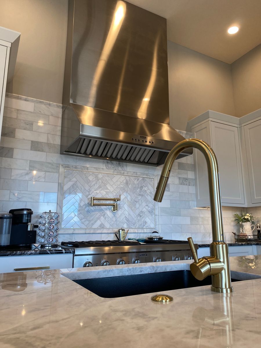 A kitchen with a stainless steel hood and a gold faucet.