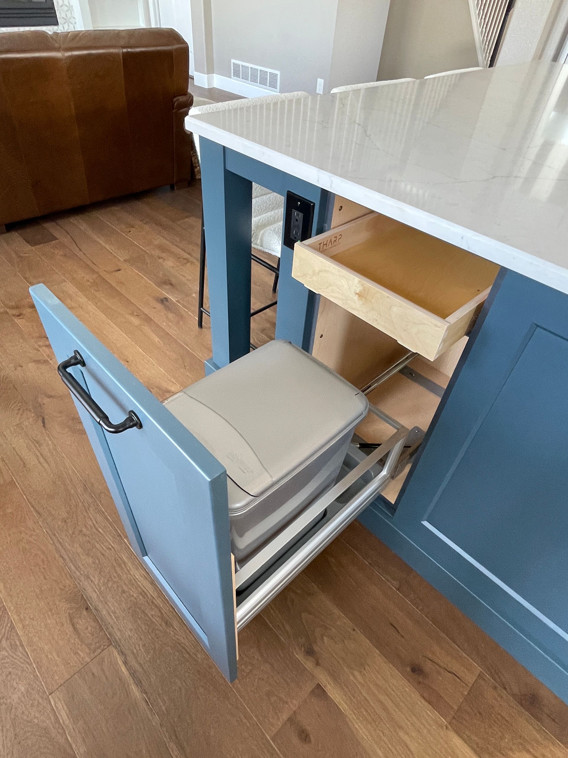 A trash can is pulled out of a drawer in a kitchen.
