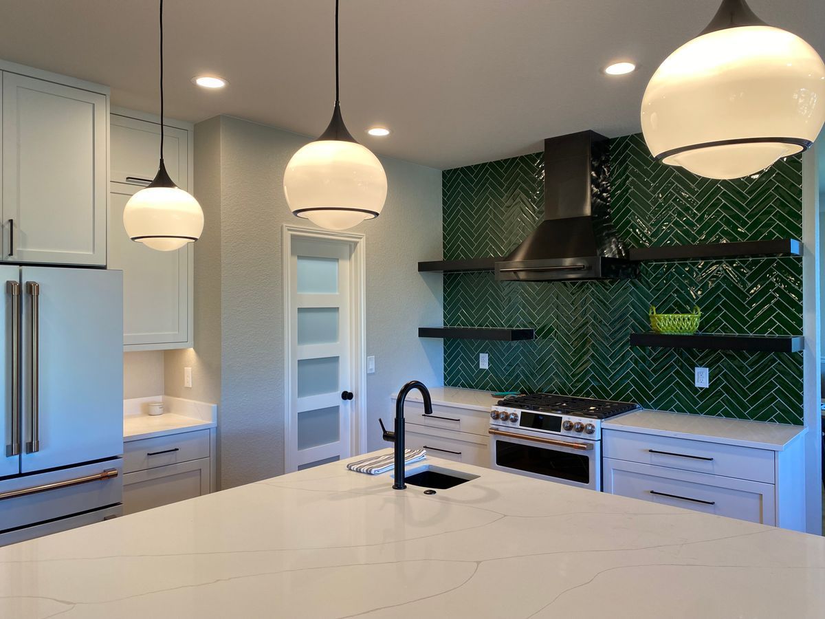 A kitchen with white cabinets and green tiles on the wall