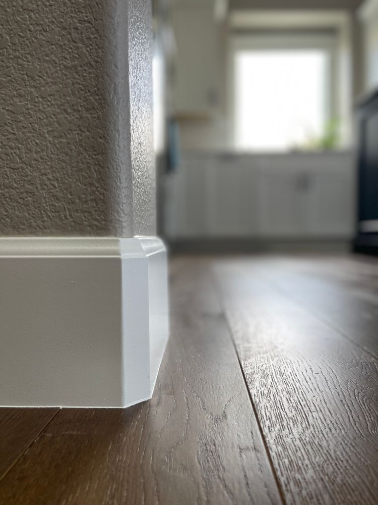 A close up of a white skirting board on a wooden floor in a kitchen.