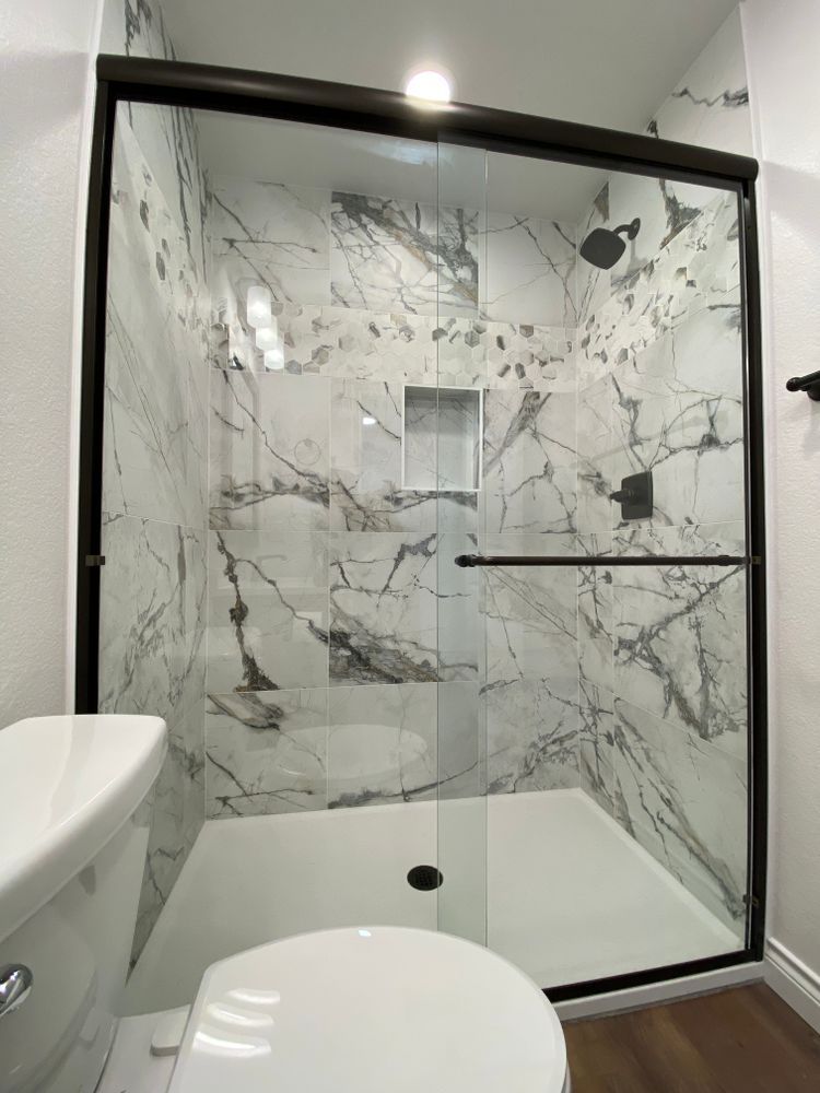A bathroom with a toilet , shower , and marble walls.