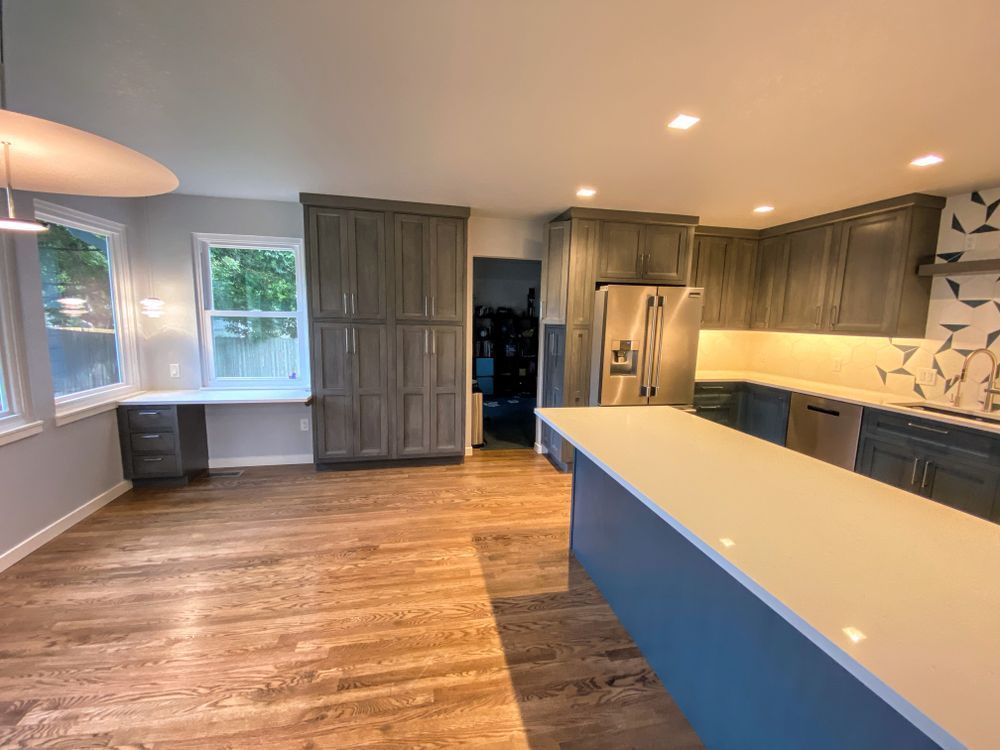 A kitchen with gray cabinets , white counter tops , and a blue island.