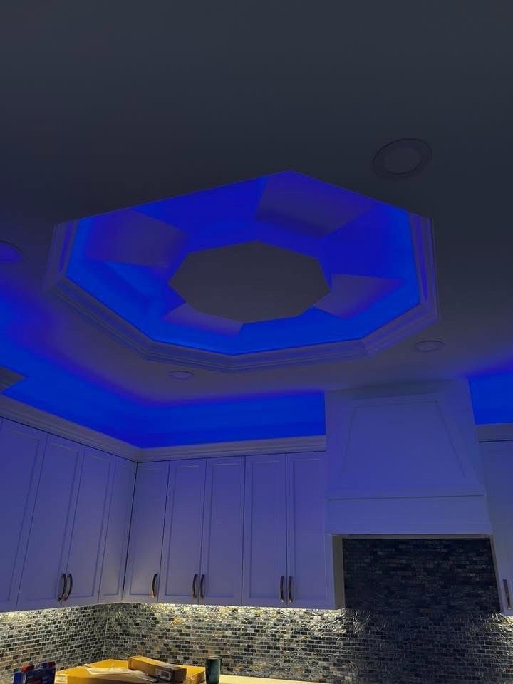 Kitchen featuring white cabinets, a stone backsplash, and an octagonal ceiling cutout illuminated by bright blue lights.