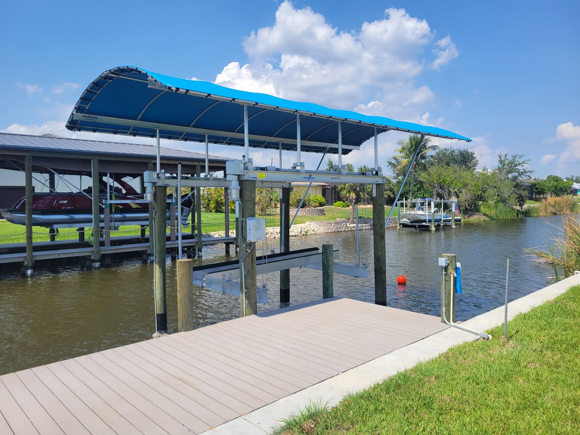 A boat lift with a blue canopy positioned over a canal next to a wooden dock on a sunny day.