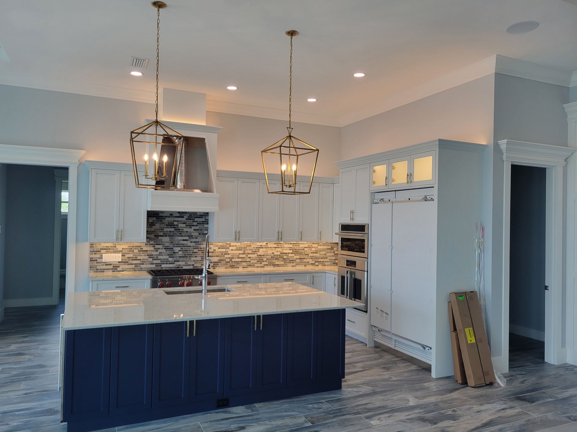 A kitchen with a dark blue island, white cabinets, stainless steel appliances, and two gold pendant lights.