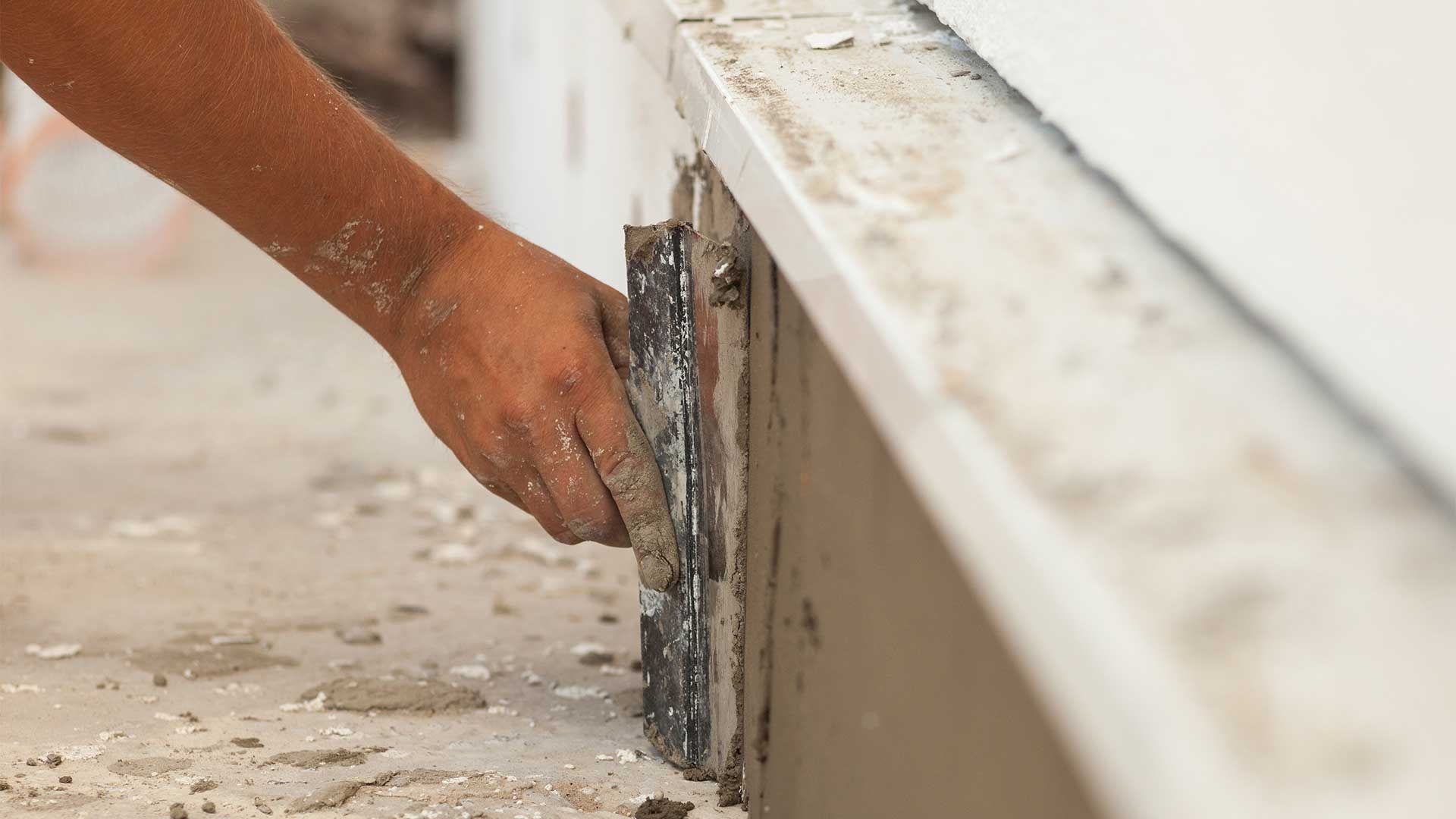 A person is plastering a wall with a trowel.