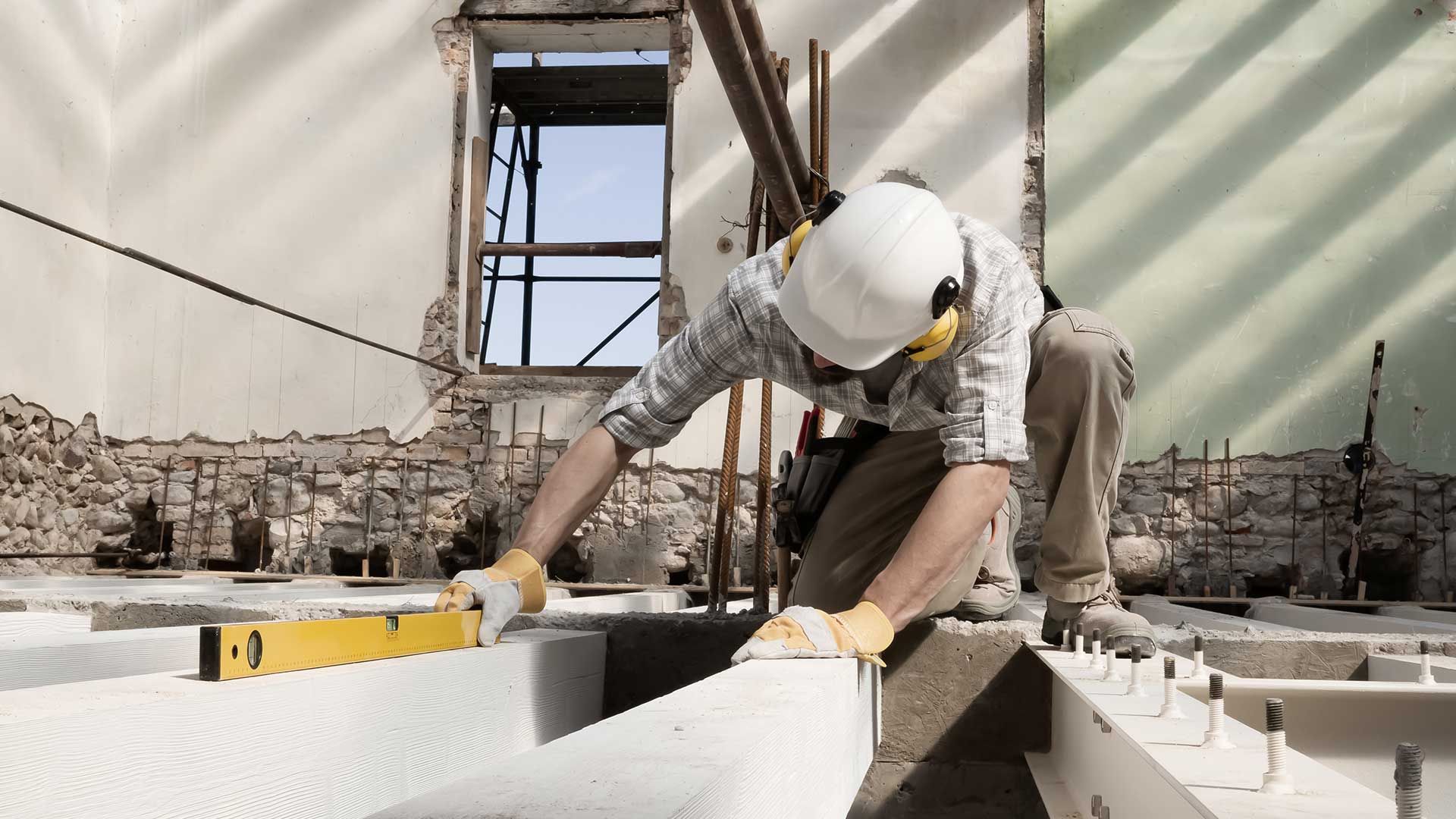 A construction worker is measuring a piece of concrete with a level.