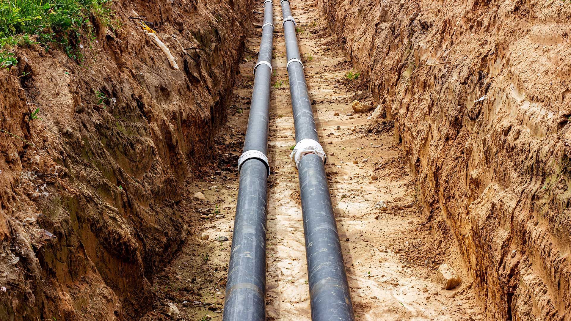 Two pipes are being installed in a trench in the dirt.