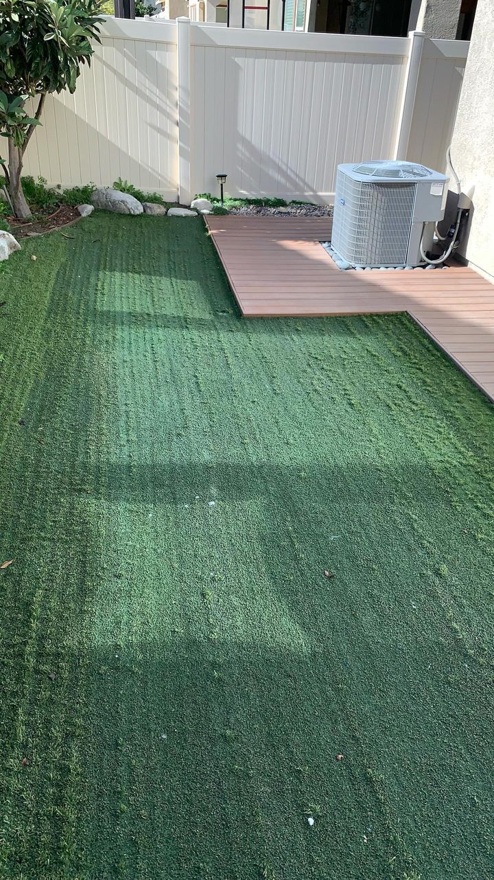 Artificial turf backyard with a wooden deck and AC unit.