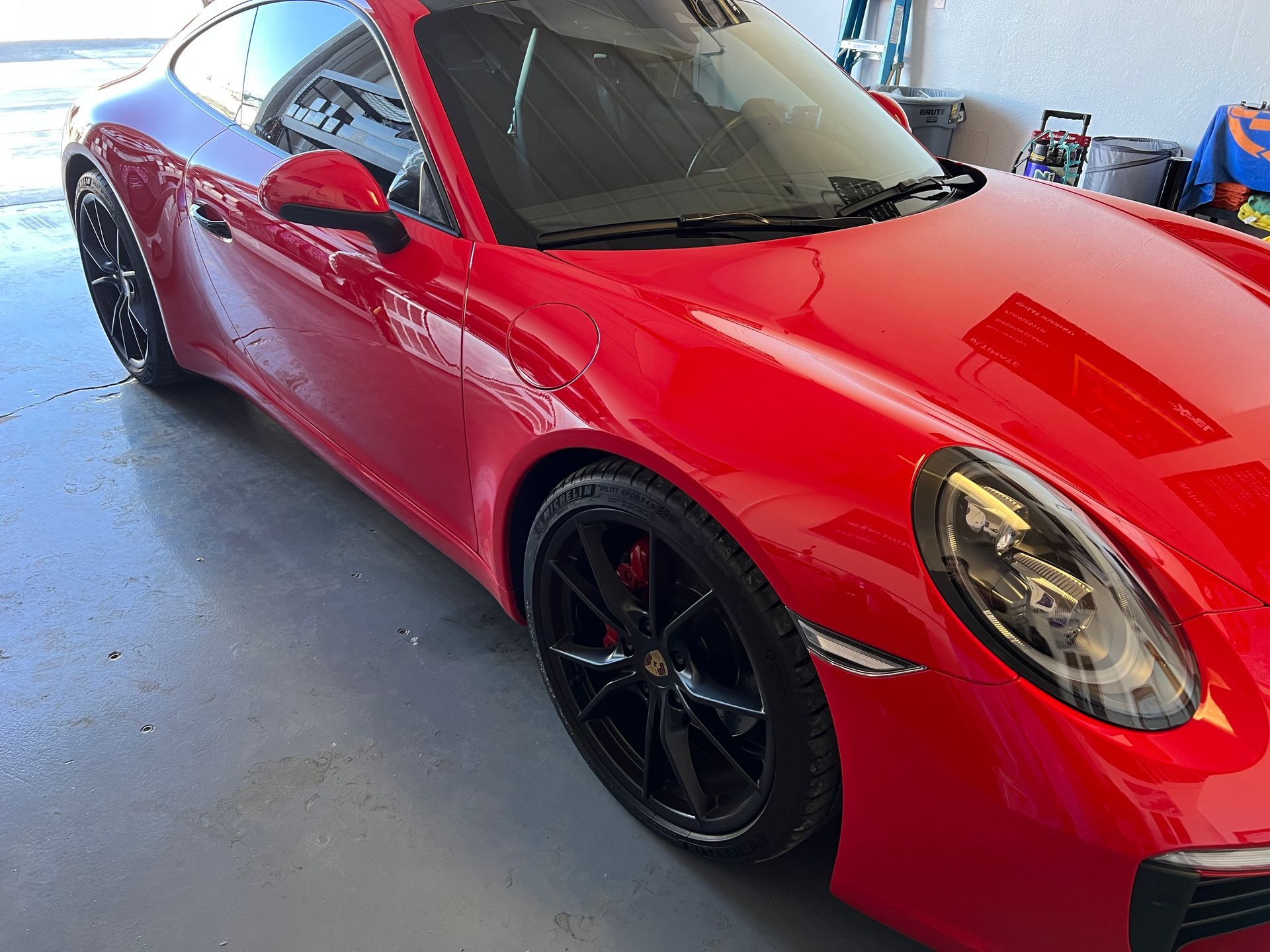 Red Porsche sports car with black rims parked in a garage.