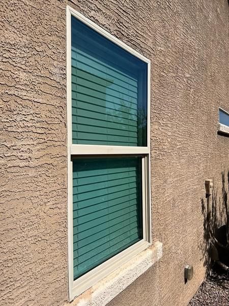 Tall window with horizontal blinds on a textured, tan wall. Beige frame.