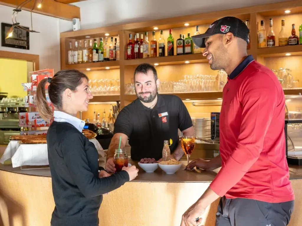 A man and a woman are standing at a bar talking to each other.