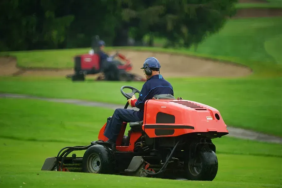 A man is riding a lawn mower on a golf course.