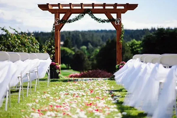 A row of white chairs are lined up in front of a wooden archway.
