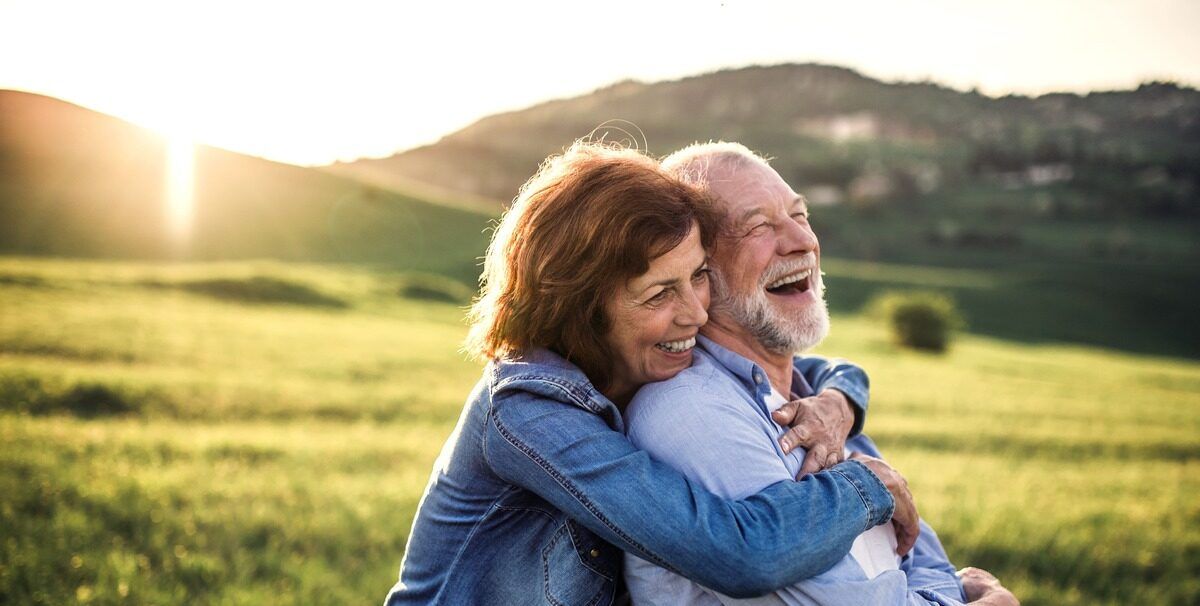 Smiling couple hugging outdoors in a sunlit grassy field with hills in the background