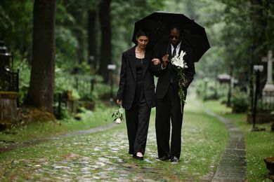 Two people in black suits walk under an umbrella