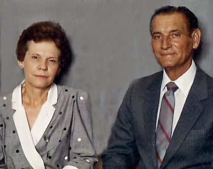 Two people seated against a plain gray background, wearing formal attire and looking at the camera.