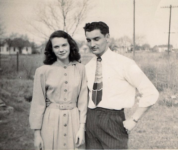 Two people standing outdoors in a black-and-white portrait, with trees and utility poles in the background.