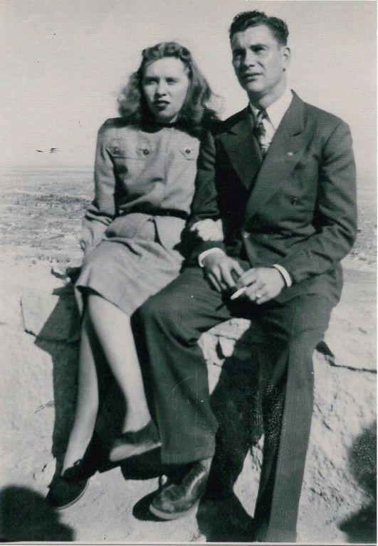 Two people seated on a stone ledge outdoors, dressed formally in a black-and-white portrait.