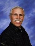 Smiling man in a dark shirt against a blue studio backdrop