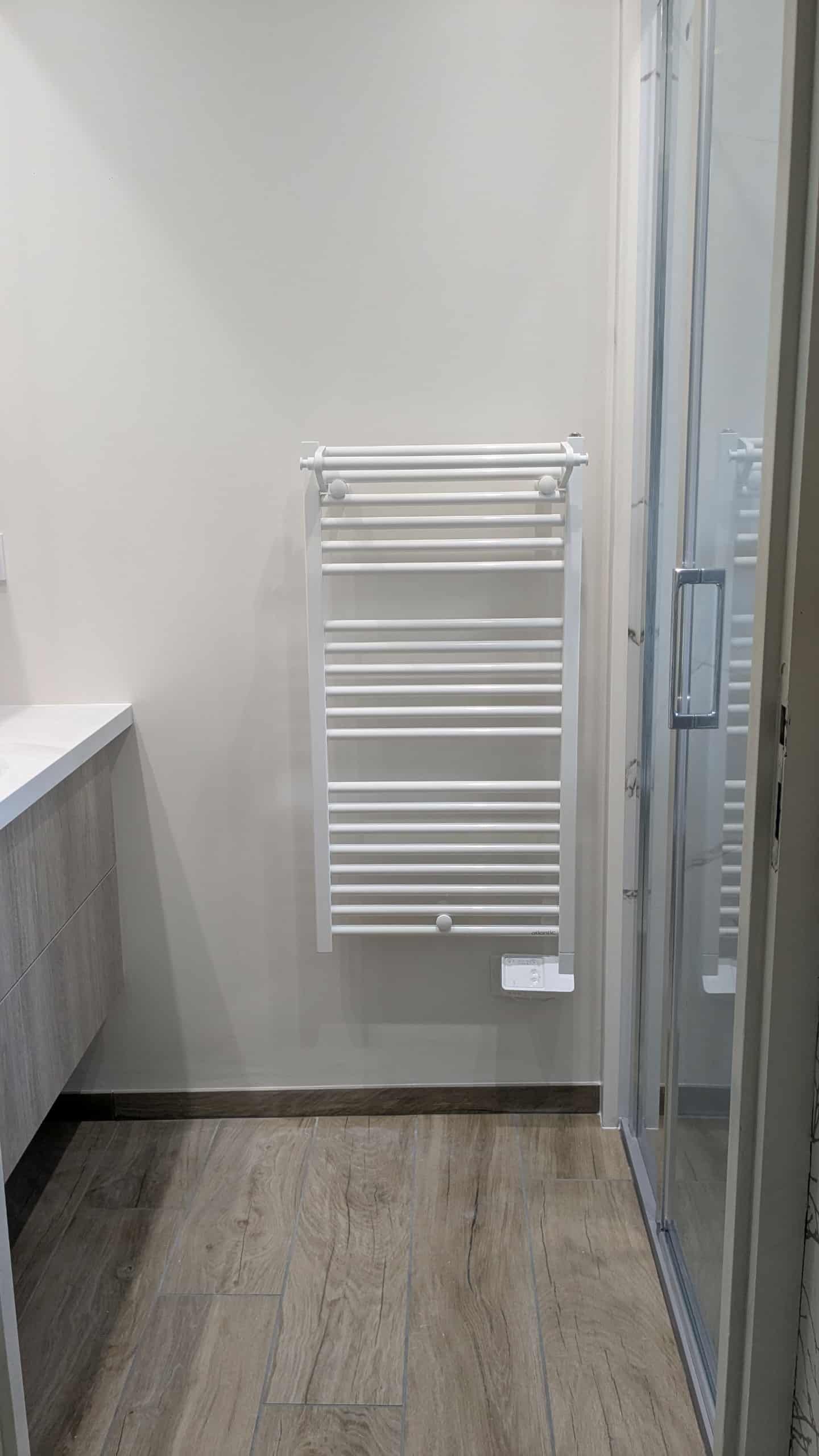 Coin salle de bains avec un sèche-serviettes mural blanc à côté d'une porte de douche en verre et d'un sol carrelé.