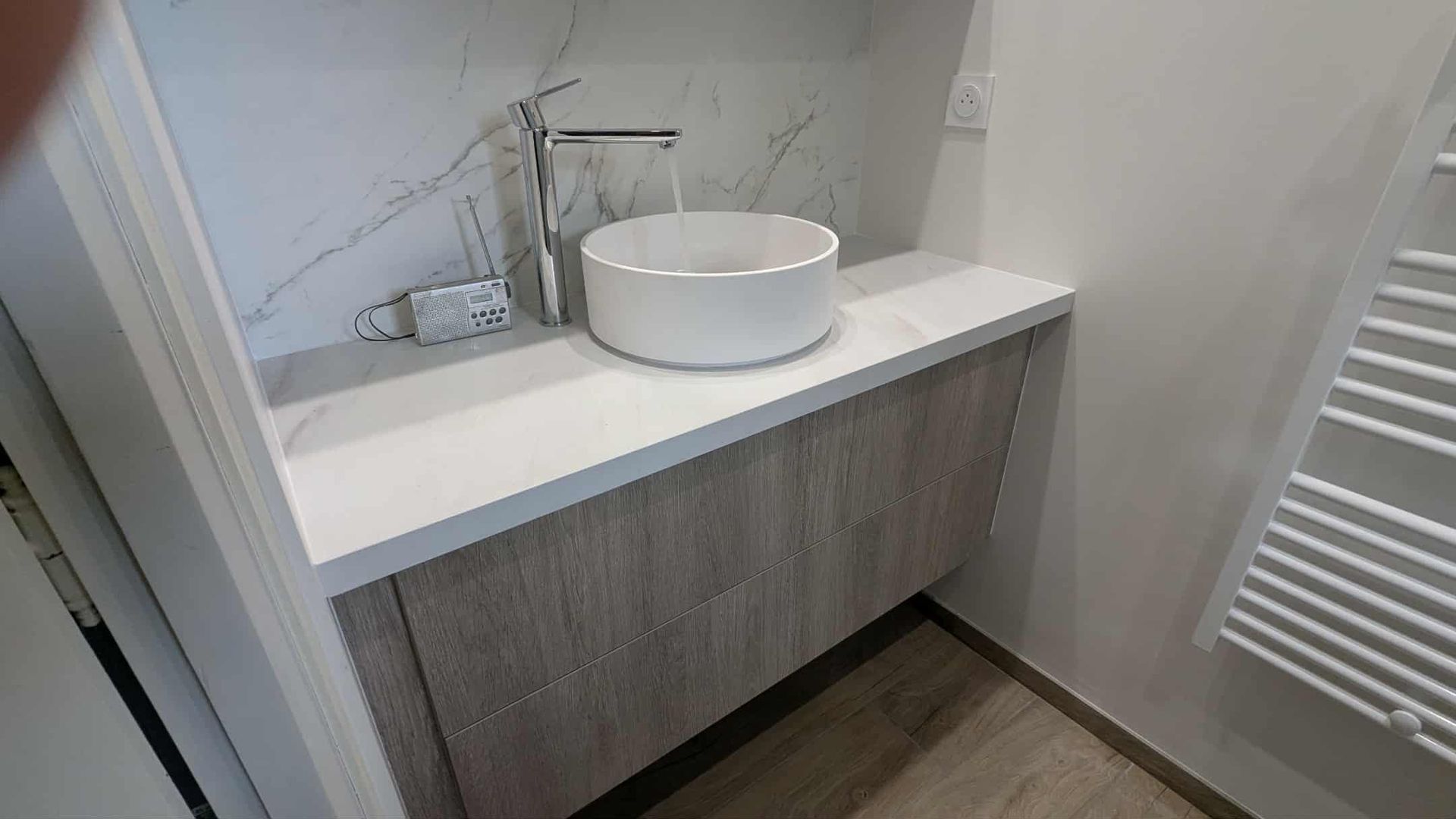 Meuble-lavabo moderne avec lavabo blanc, armoire grise et sèche-serviettes sur la droite.