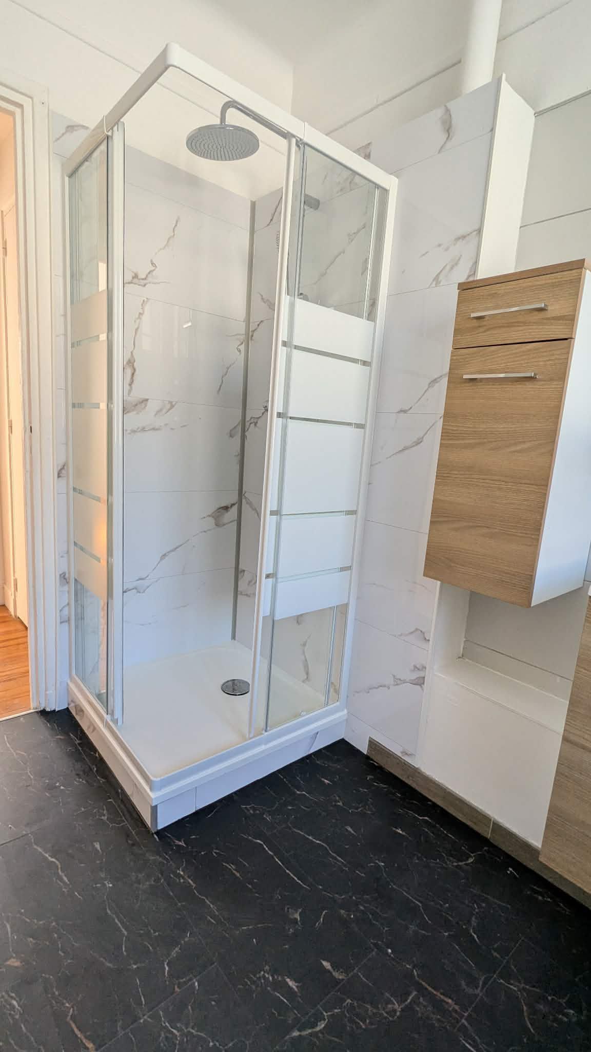 Cabine de douche moderne en verre avec murs carrelés blancs et sol à motifs noirs dans une salle de bains