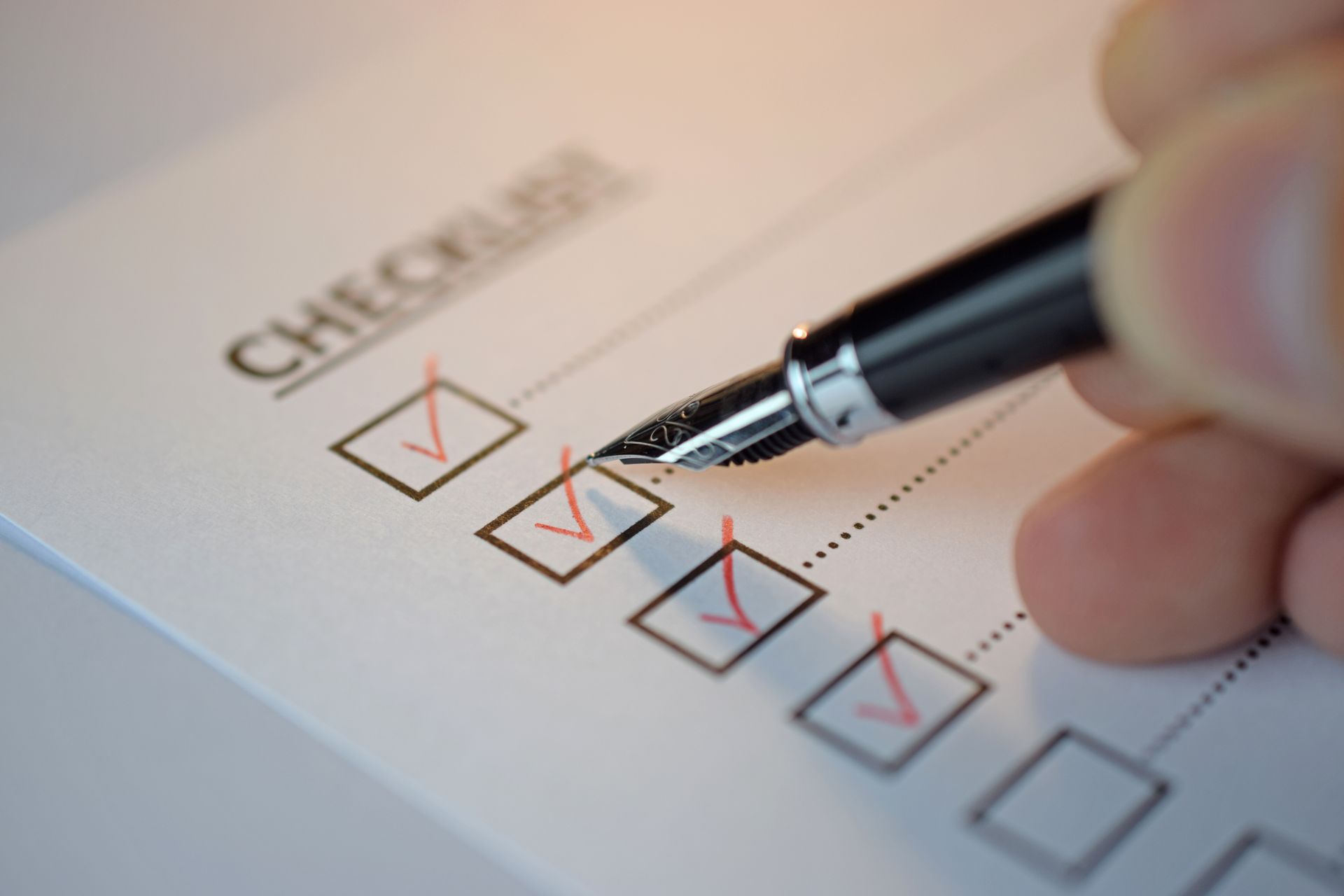 Hand with pen checking boxes on a checklist.