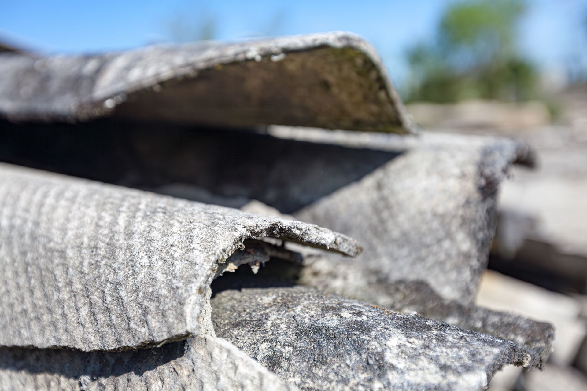 Close-up of weathered gray asbestos roof tiles, curled edges, exterior setting.