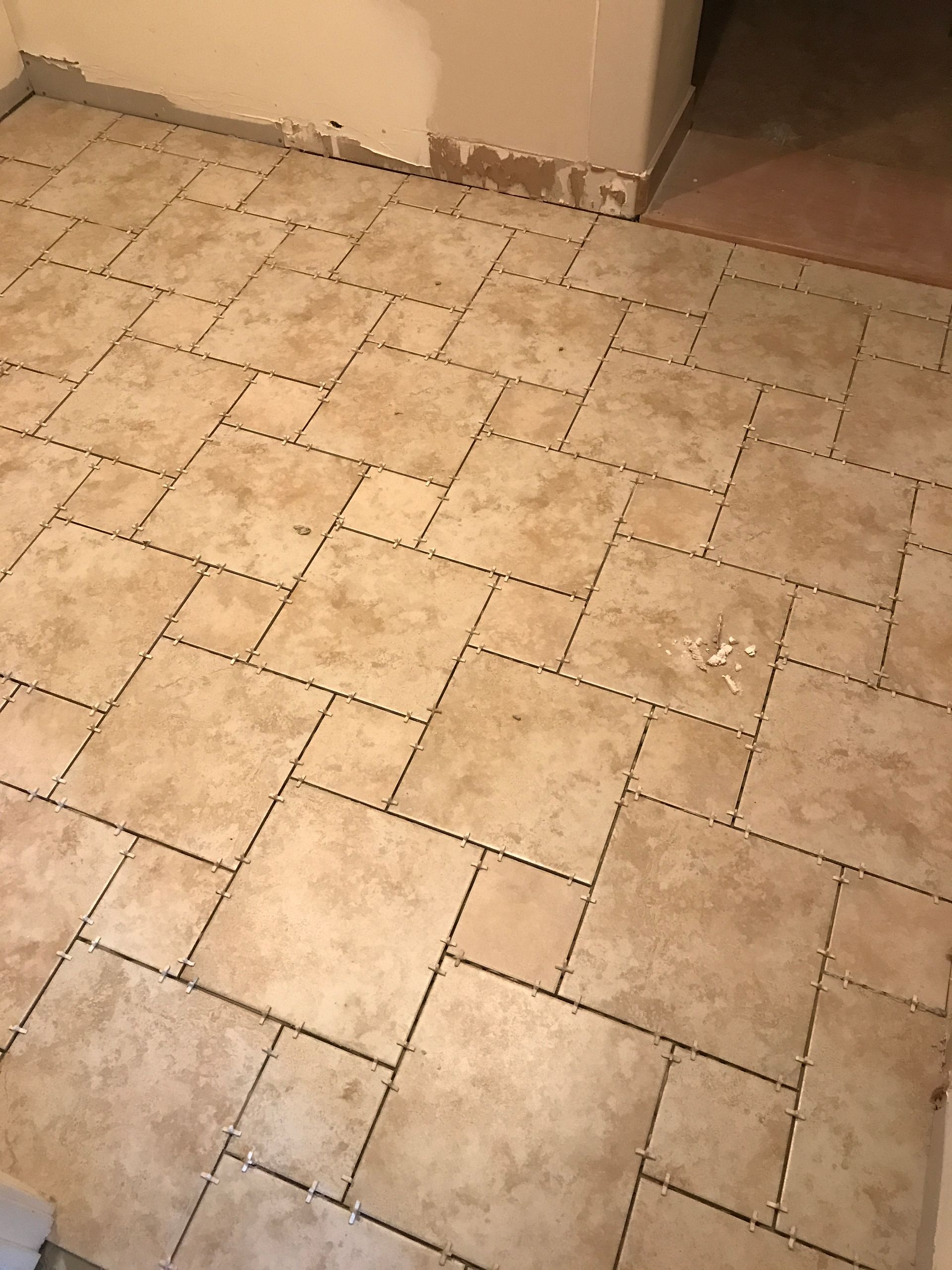 Beige tiled floor with a corner wall and baseboard, viewed from above.
