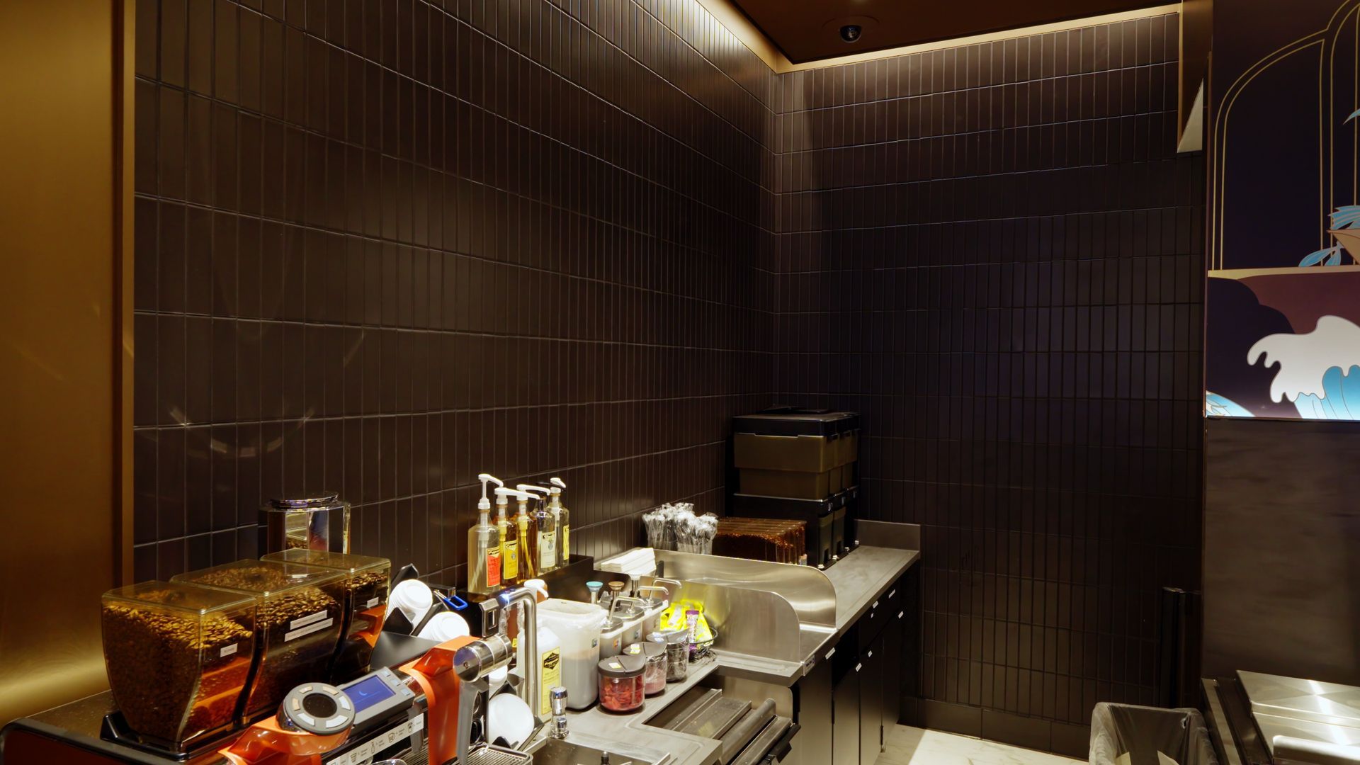 Dim lounge bar with dark walls, backlit ceiling, and a cluttered counter with bottles and drinkware.