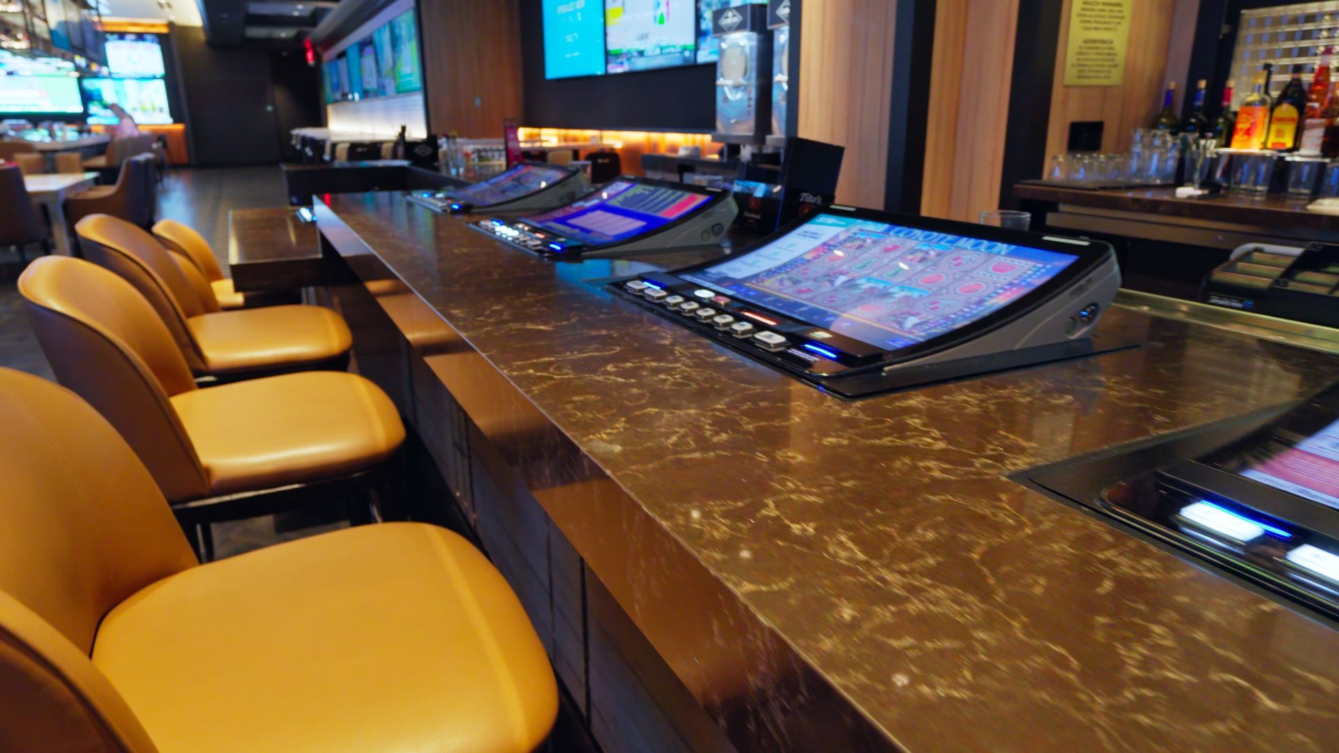 Empty casino gaming tables with glowing touchscreens and yellow stools in a dimly lit lounge