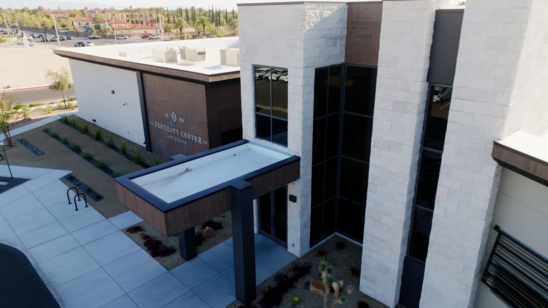 Modern building exterior with white and brown facades, tall windows, and a covered entrance walkway