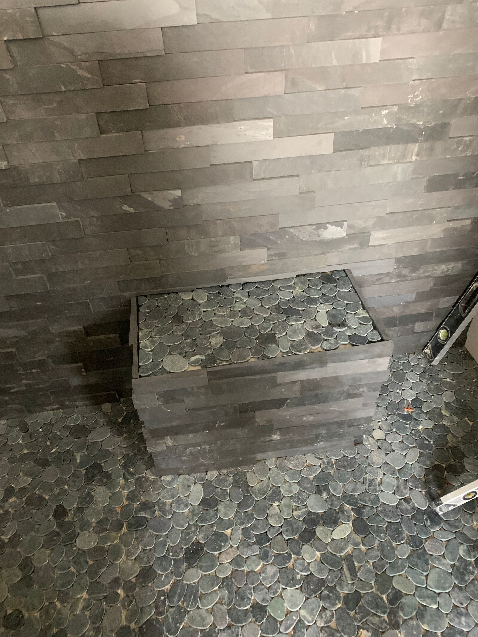 Small stone bench in a tiled corner with a textured brick wall and mosaic floor.