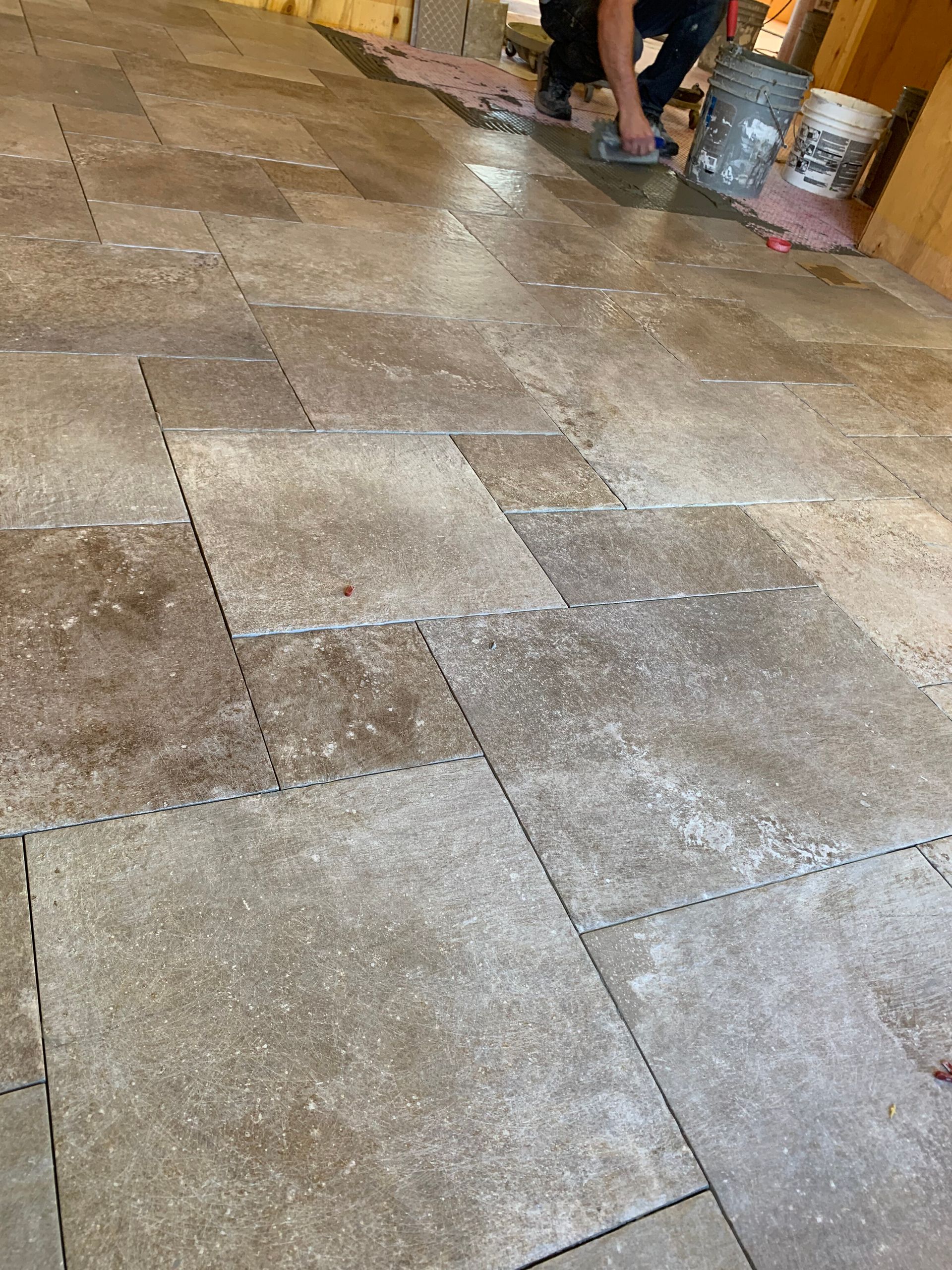 Stone-tiled floor with a person’s feet near the top edge and a backpack in the background