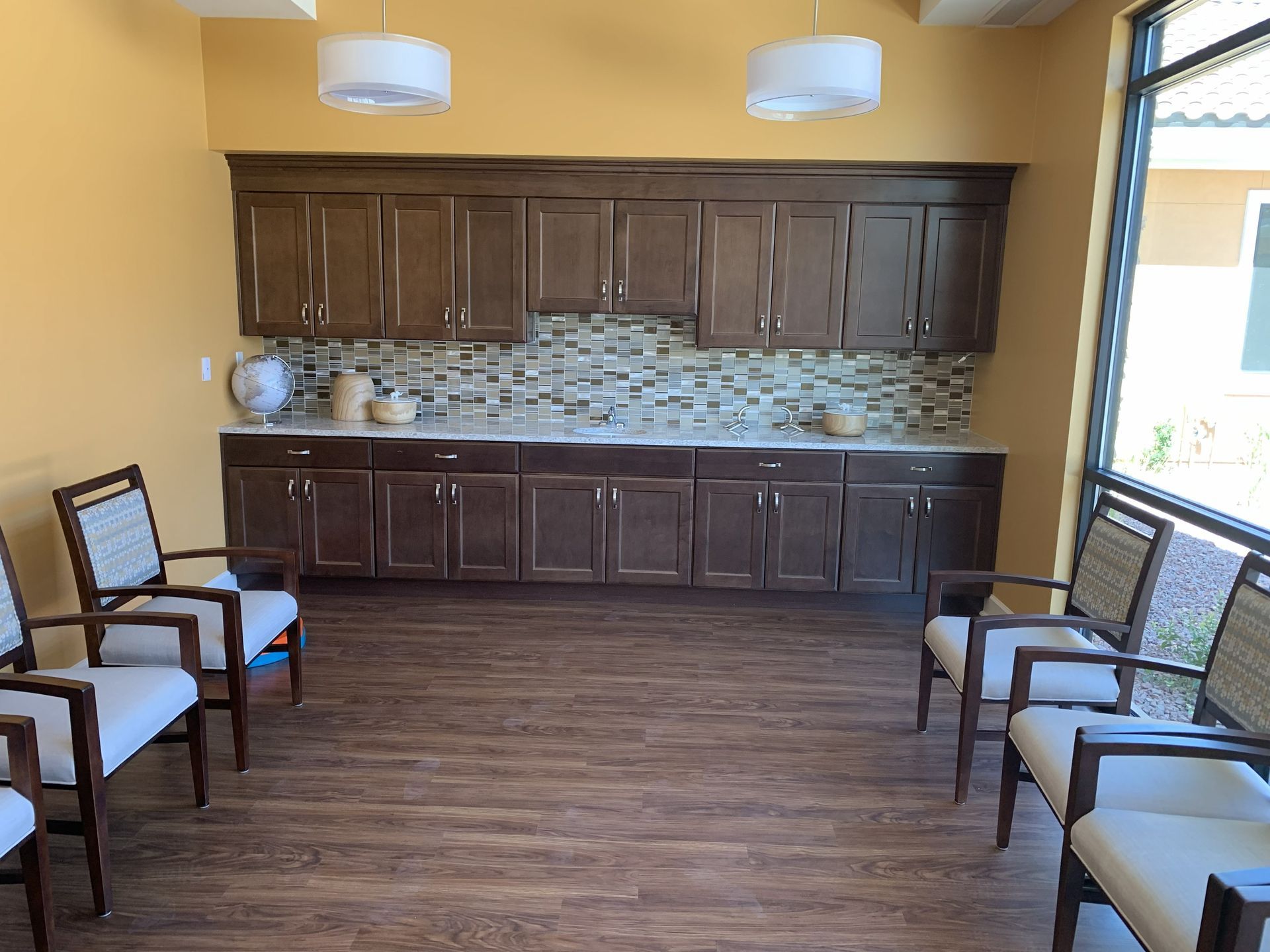 Community room with wooden cabinets, mosaic backsplash, and chairs arranged along the walls