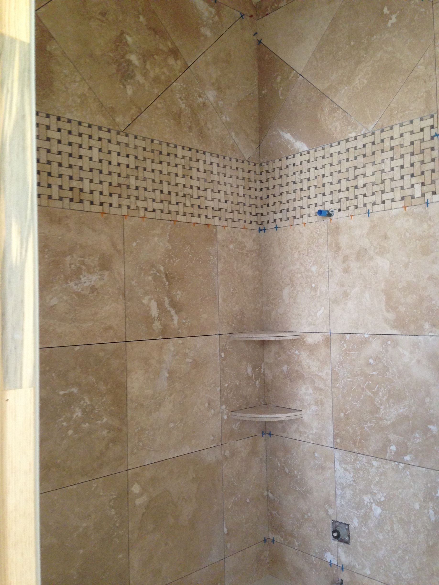 Walk-in shower with beige tile walls, mosaic accent band, and built-in corner shelves