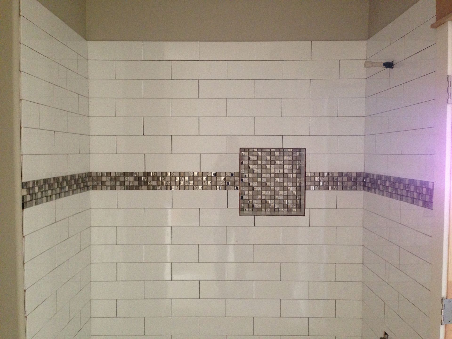 Tiled shower wall with a horizontal mosaic accent and square decorative inset shelf/feature.