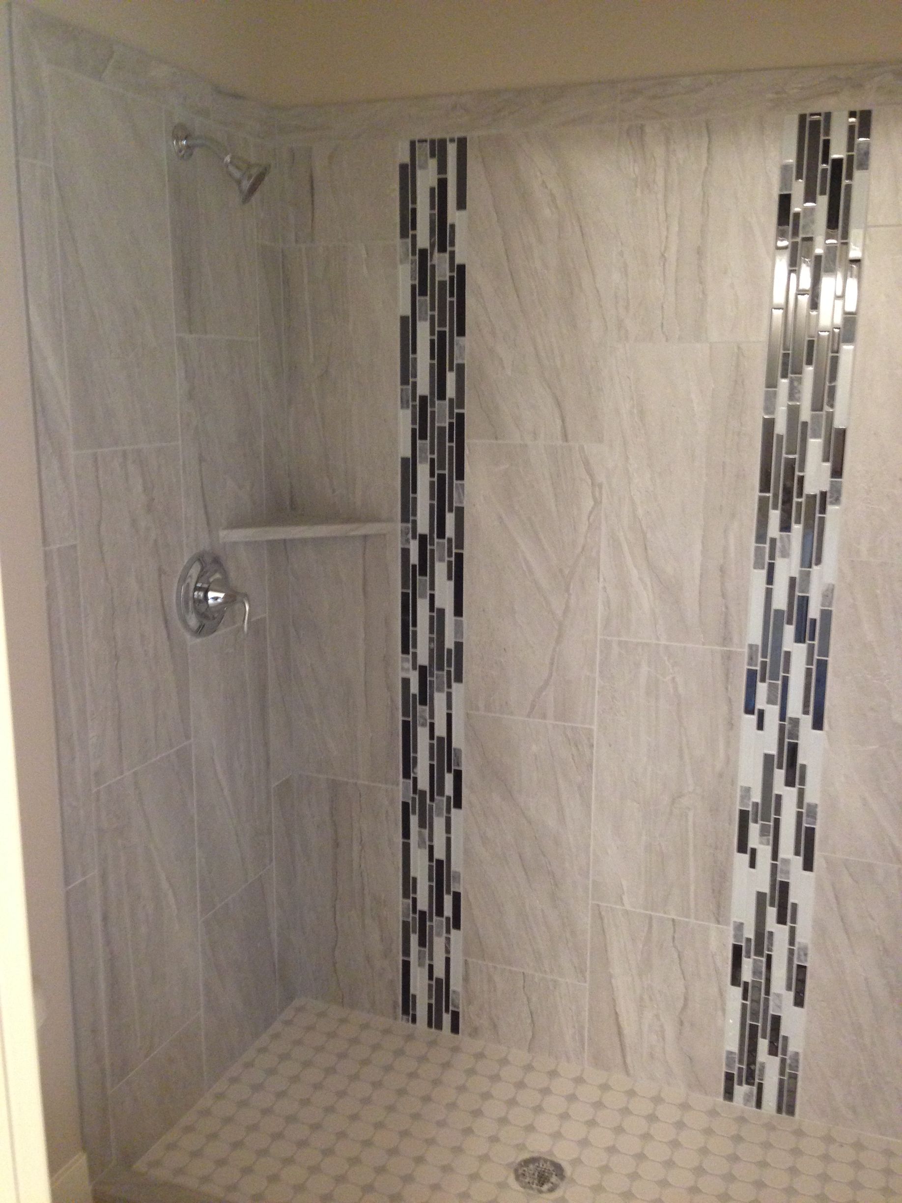 Tiled walk-in shower with mosaic accent strips, showerhead, and tiled floor with drain.