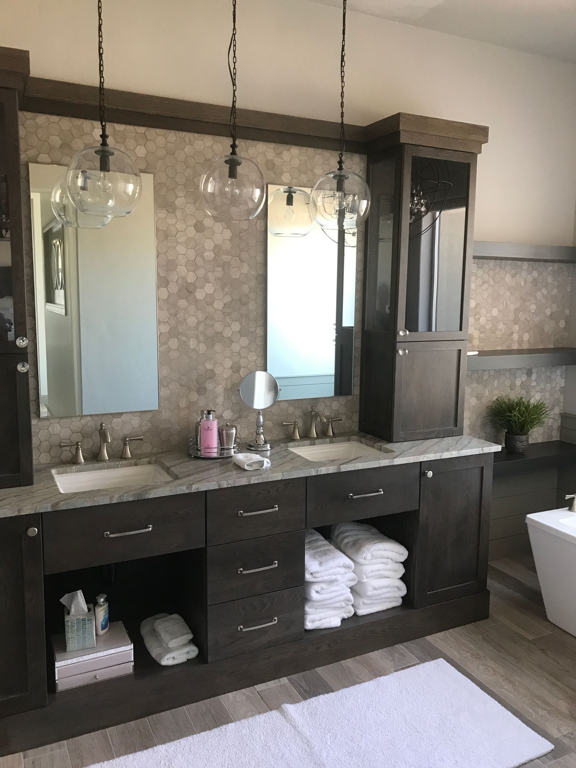 Dark bathroom vanity with double mirrors, sinks, open storage shelves, and folded towels.