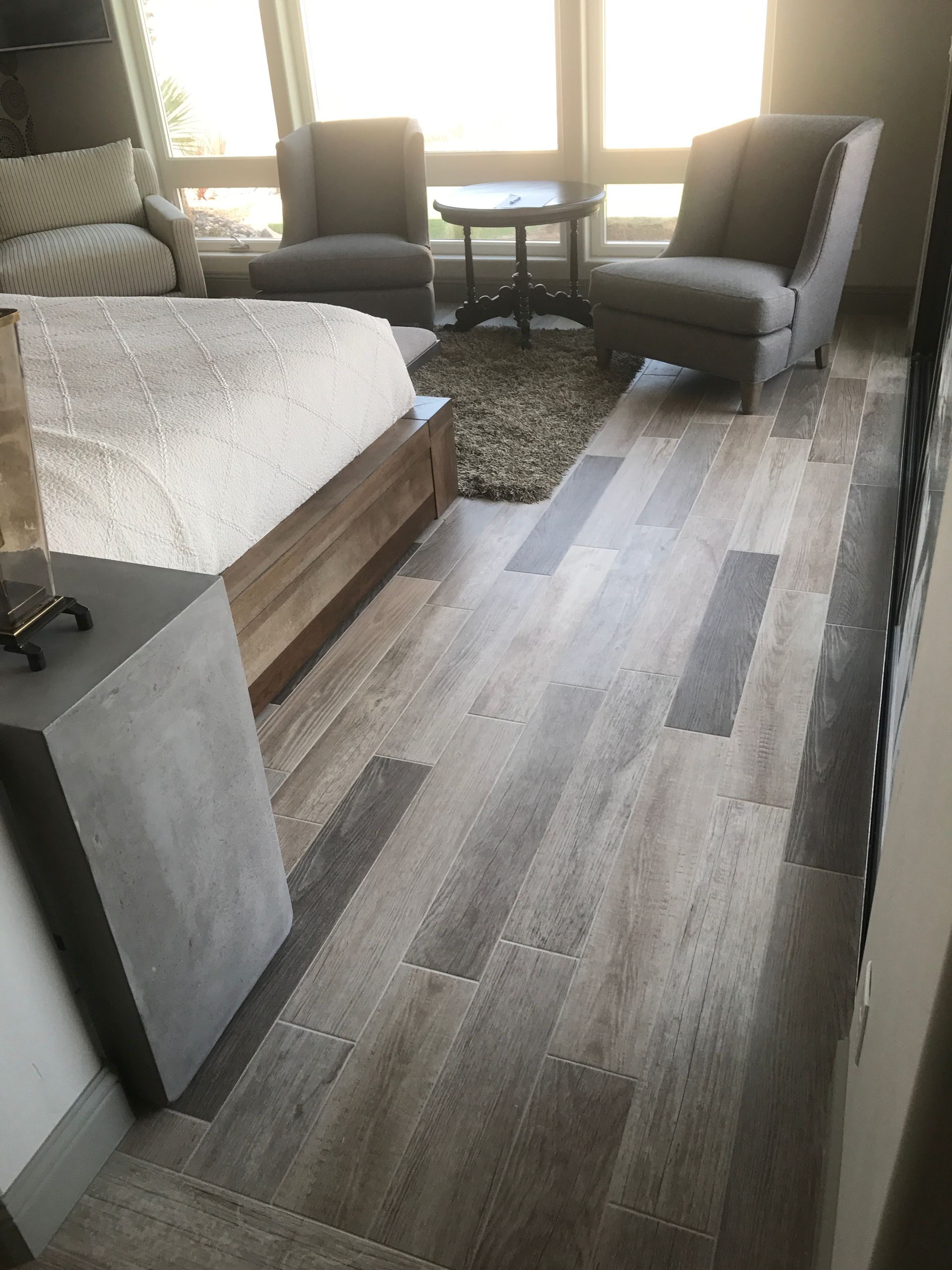 Cozy living room with gray chairs, small table, bed, and light wood flooring by a bright window