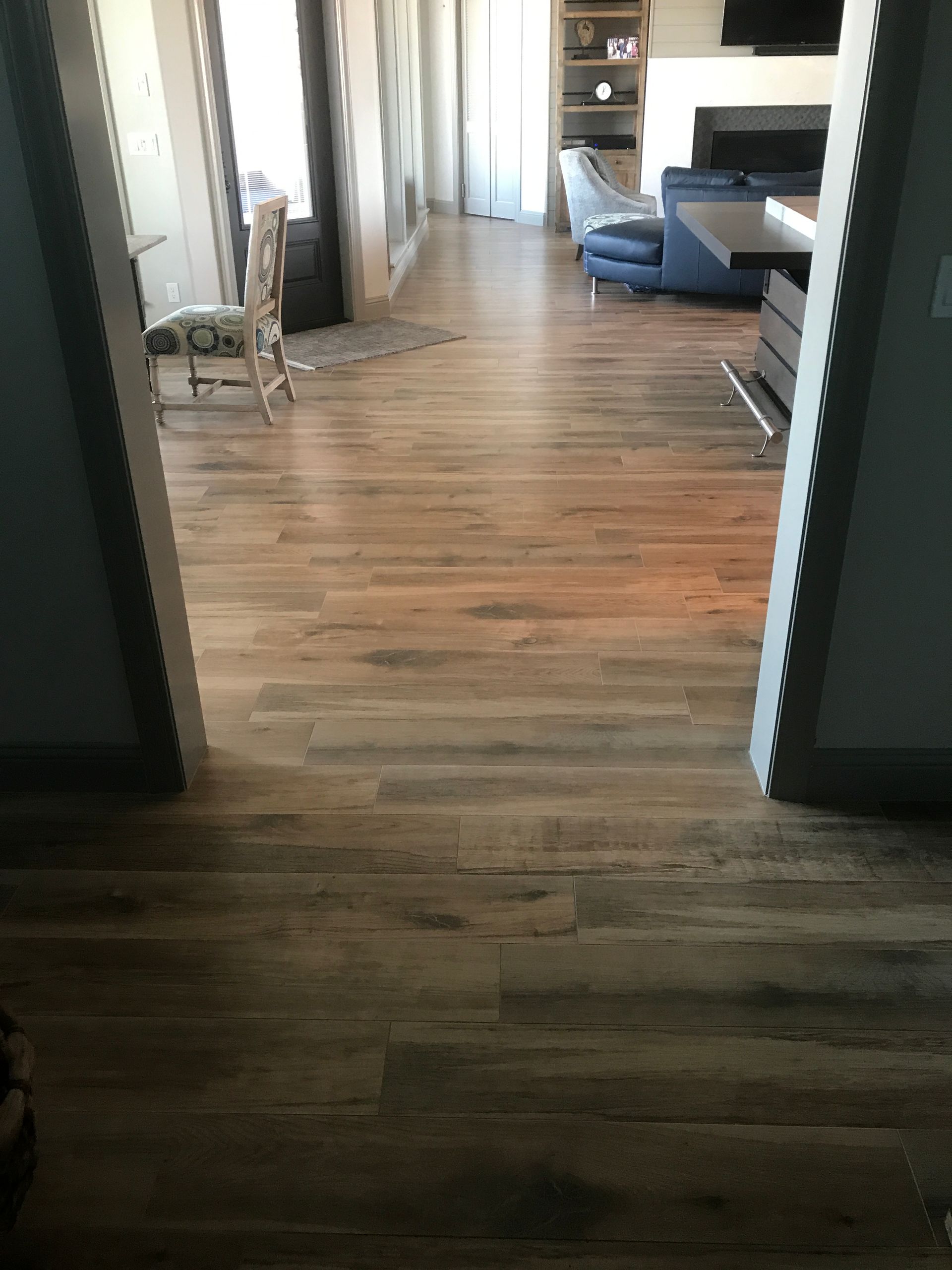 Empty hallway with hardwood floors, leading to a bright living room with a blue sofa.