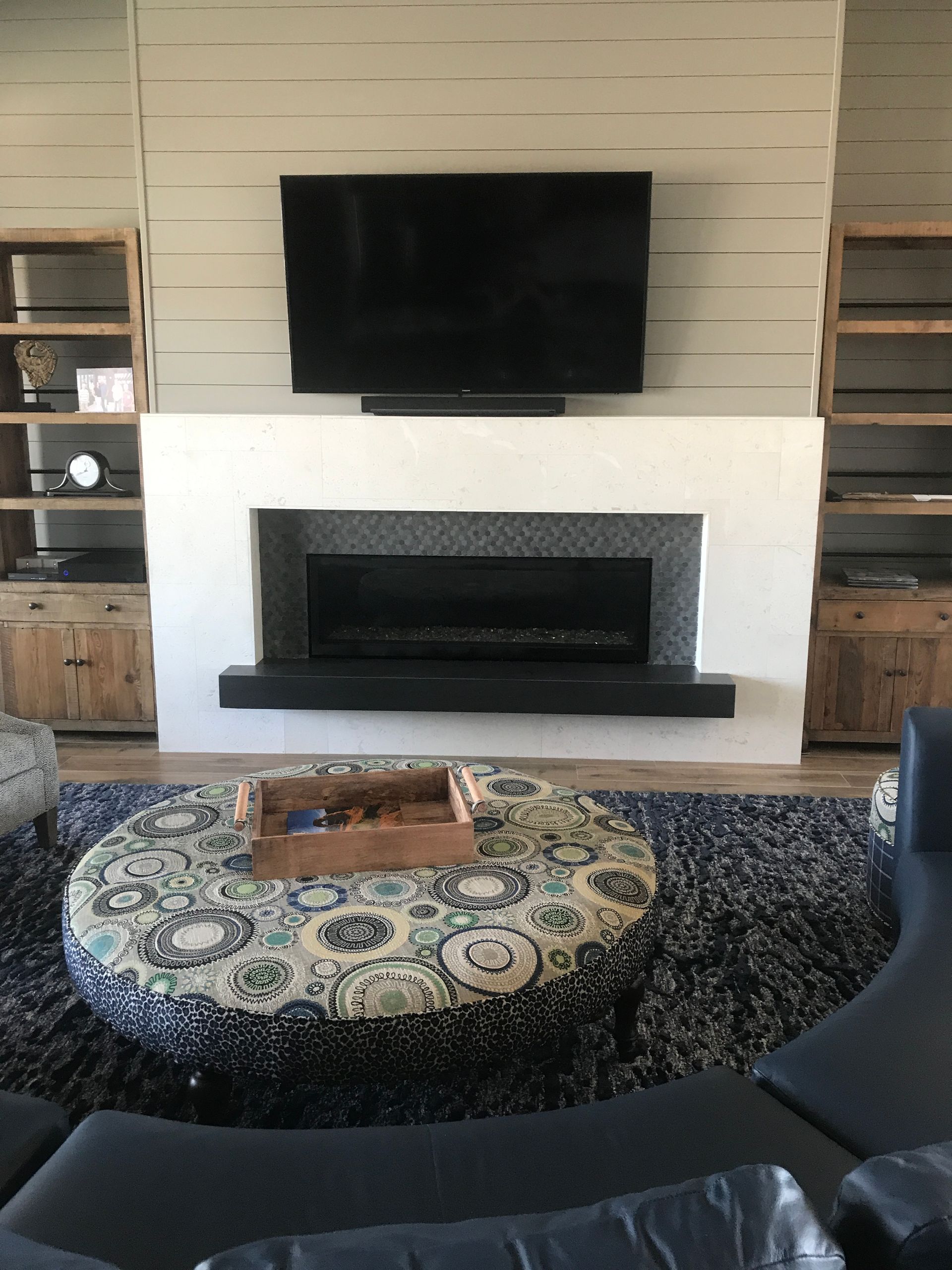 Modern living room with wall-mounted TV, fireplace, and patterned round rug around a coffee table.