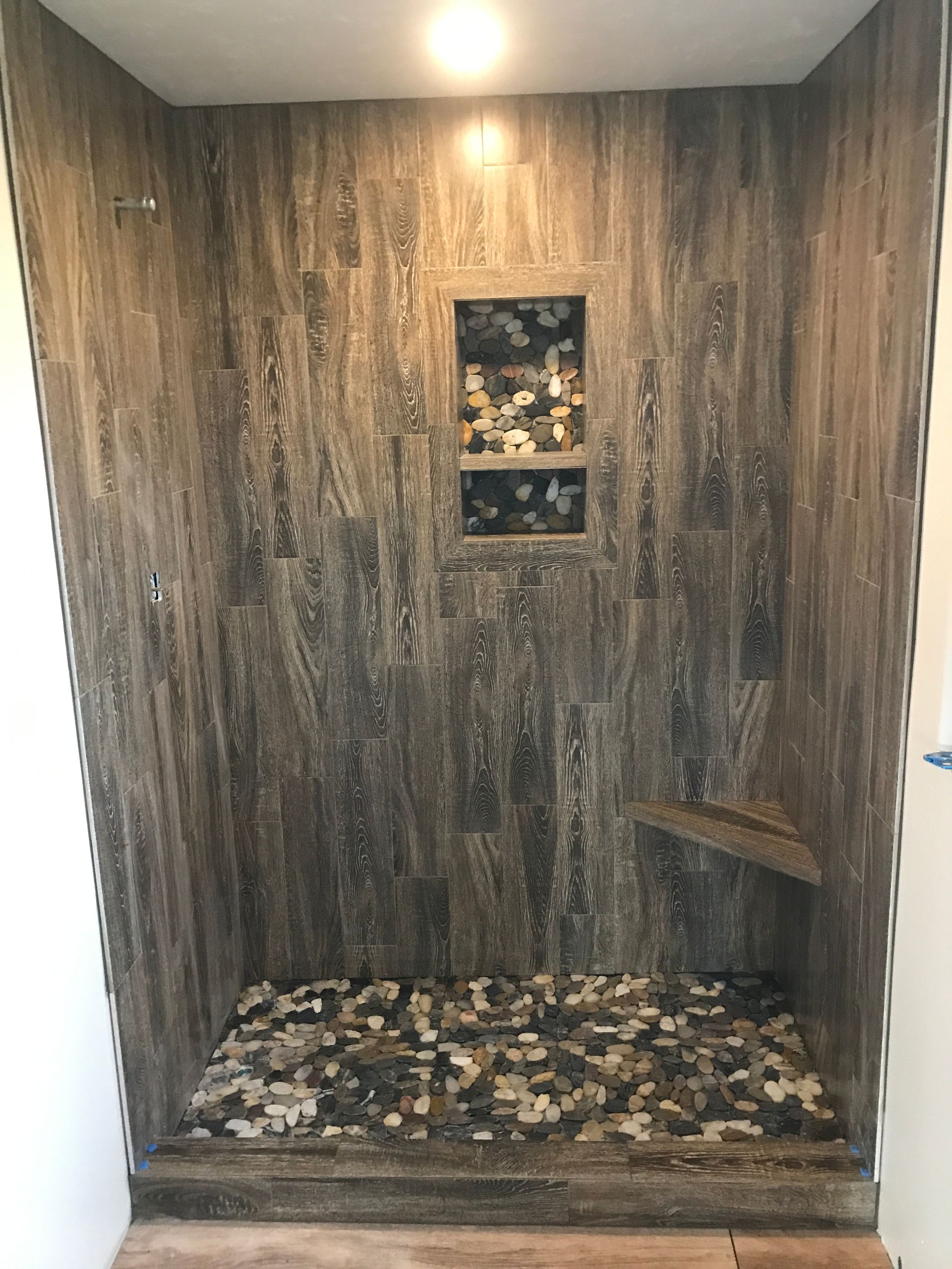 Small wood-paneled shower stall with mosaic stone floor, small wall niche, and built-in bench on the right.
