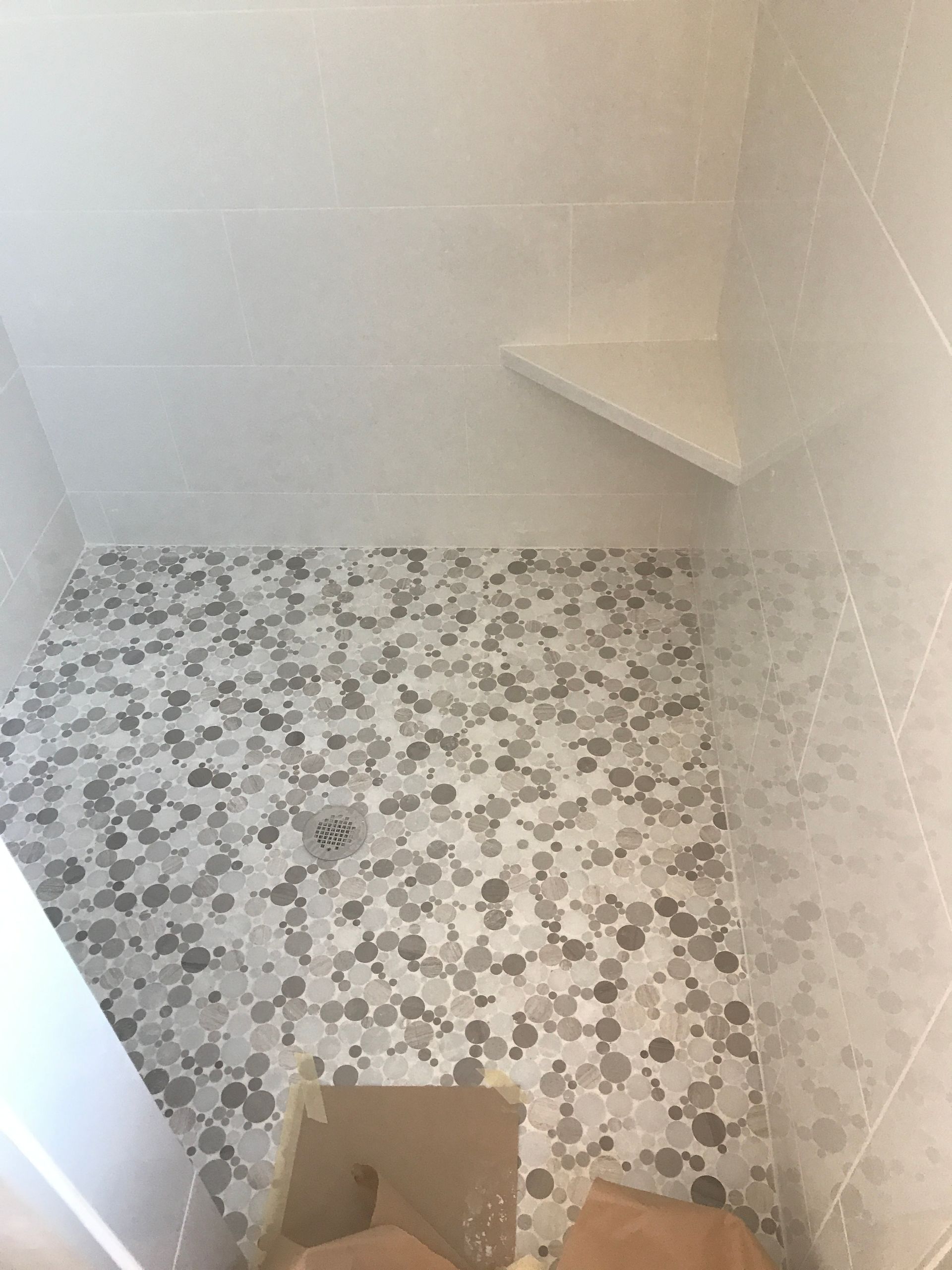 Empty tiled shower with mosaic floor, corner shelf, and drain opening.